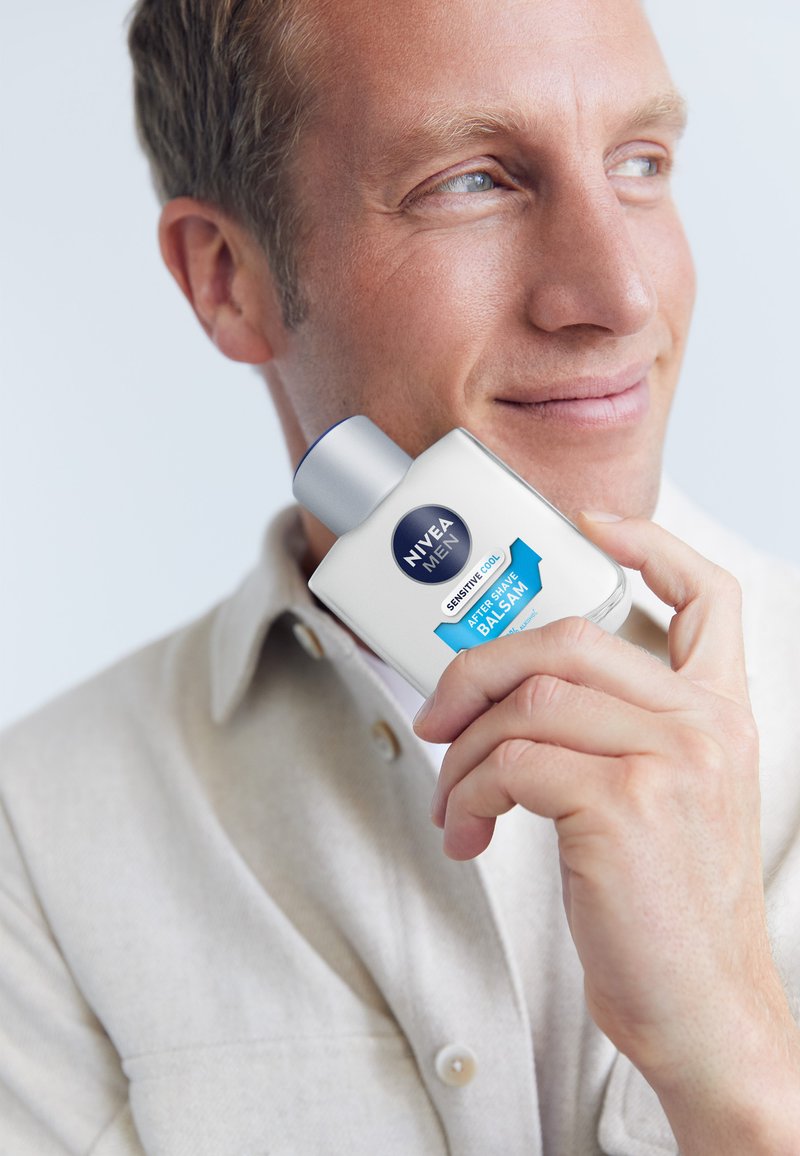 Nivea Men Sensitive Cool After Shave Balsam, weiße Flasche mit blauen Akzenten, silberner Deckel, von einer Person gehalten, glatte Textur, klar beschriftet.