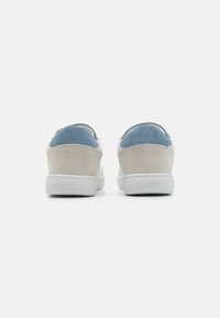 Zapatillas con una parte superior de ante gris claro y un acento de ante azul en el talón, suela de goma blanca y un diseño minimalista.