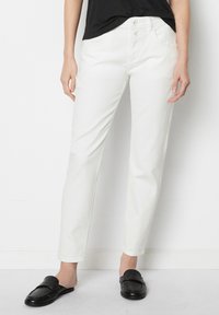 Vita, raka jeans i lättviktig bomull. Har en knappdesign i grenen, framfickor och en slät, jämn yta. Stylade med svarta loafers.