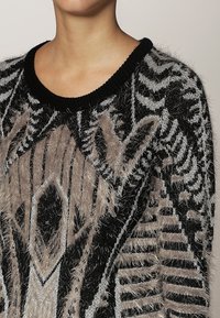 Maglione fuzzy nero e grigio con motivo geometrico testurizzato, scollatura rotonda e materiale morbido e soffice.