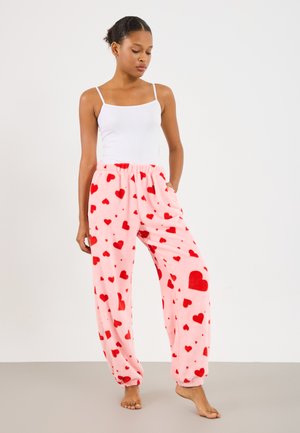 Fleece pyjamasbyxor i ljusrosa med ett röd hjärtat mönster, med en elastisk midja och vida ben för komfort.
