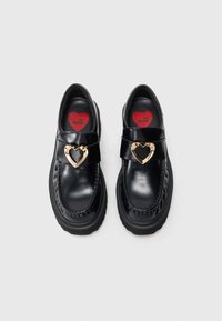 Juodi odiniai loaferiai su apvaliu pirštu, su aukso spalvos širdelės formos sagtimi ir kontrastinga tekstūruota padanga. Raudoni pado pamušalai su logotipu.