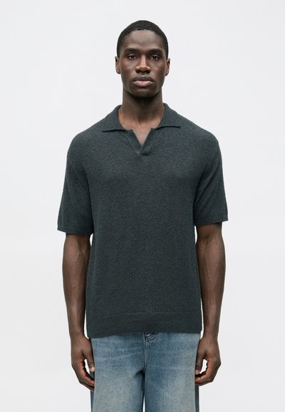 Polo en maille à manches courtes gris foncé avec une finition texturée et un col en V. Associé à un jean denim bleu clair.