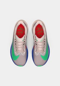 Nike-Laufschuhe mit einem Netz-Obermaterial, das in einem pink- und grau-Farbschema gehalten ist, mit grünen Akzenten und blauen Sohlen. Der Text auf den Innensohlen ist sichtbar.