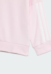 Svetloružová mikina s rebrovanými manžetami a bielym prúžkovým dizajnom po stranách rukávov. Mäkká textúra a voľný strih.