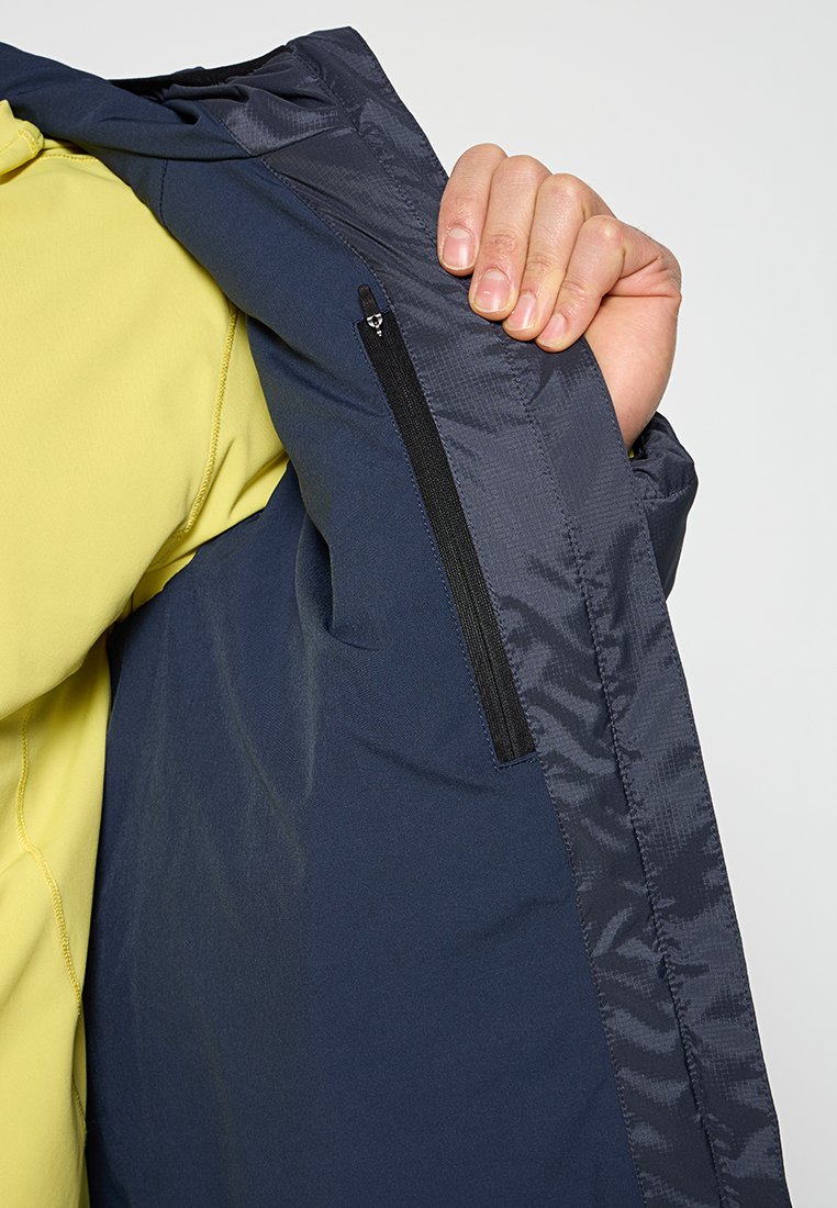 Intérieur de veste bleu marine avec une texture lisse, présentant une poche zippée sur le côté gauche. La couche extérieure a un léger éclat.