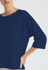 Navy-blaues Oberteil aus glattem Stoff, mit weitem Ausschnitt und Dreiviertelärmeln, entworfen in einem lockeren Schnitt.