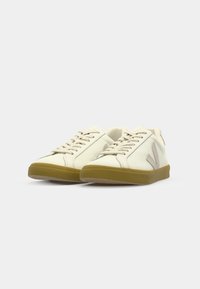 Hvit sneakers med glatt skinnoverside, beige detaljer, flate snørebånd og såle av gummigummi. Inkluderer logodetaljer på sidene.