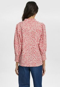 Blusa floreale rossa e bianca con collo alto, maniche a sbuffo e orlo curvo. Realizzata in tessuto leggero con una texture morbida.