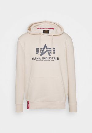 Bežová mikina s kapucňou a šnúrkou, prednou vreckou. Obsahuje tmavosivý logo a text "ALPHA INDUSTRIES" spolu s červeným akcentom na leme.