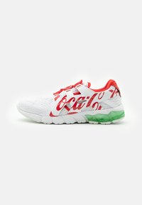 Vit sportskor med röda detaljer och strukturerad mesh-ovandel. Har en framträdande röd Coca-Cola-logotyp och en grön genomskinlig sula.