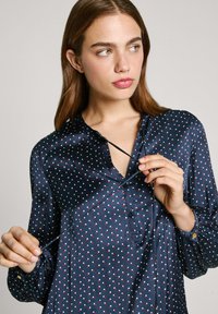 Μπλούζα ναυτικού τύπου από σατέν, με λευκές και κόκκινες πουά, κουμπιά μπροστά και ελαφρώς σ gathered μανίκια. Διαθέτει χαλαρή γραμμή και γιακά.