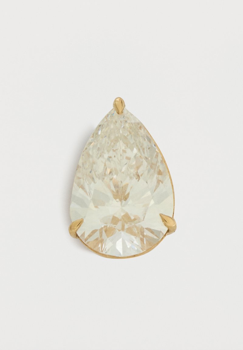Διαφανές πετράδι σχήματος δακρύου με χρυσή βάση με νύχια σε λευκό φόντο.