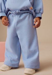 Lyseblå sweatpants med løs pasform, elastisk talje og snøre. Har labeldetaljer på siden og blød fleece-tekstur.