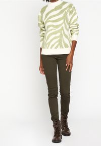 Suéter de punto en color crema con rayas de cebra verde, combinado con pantalones verde oliva y botas de tobillo marrones con cordones y detalle de correa.