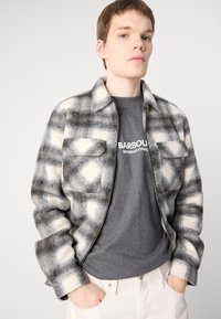 Gray and white checkered shirt jacket in wool blend, featuring a zip closure, two chest pockets, and a slightly textured surface.