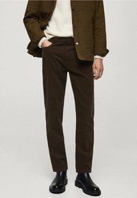 Bruine corduroy broek met een slim fit, gecombineerd met een crèmekleurige trui en een olijfgroene jas. Zwarte leren laarzen maken de outfit compleet.