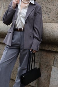 Pilkas pritaikytas švarkas ir plačių kojų kelnės, derinamos su juostelėmis raštuota marškinėliais, juodu odiniu rankiniu krepšiu ir perlais. Lygaus audinio tekstūros.