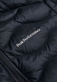 Black puffer jacket with quilted texture, featuring a zipper and white "PeakPerformance" logo embroidered on the chest area.