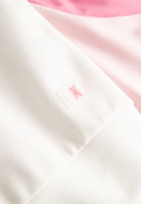Close-up van gevouwen witte en roze stof met een klein roze dierenlogo op een wit label dat aan de witte stof is bevestigd.
