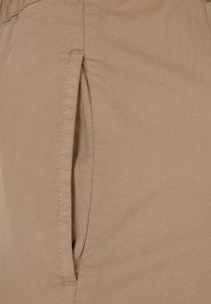 Pantalons beiges en tissu lisse et texturé, dotés d'une poche latérale et d'une taille ajustée. Des coutures détaillées renforcent la durabilité.