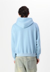 Sweatshirt cu glugă de culoare albastru deschis, cu o croială lejeră, având manșete și tiv din material rib elastic, fabricat dintr-un material moale cu o textură netedă.