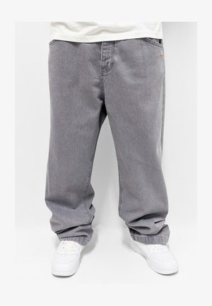 Graue Jeanshose mit lockerer Passform, ausgestattet mit genähten Taschen und elastischen Bündchen. Kombiniert mit weißen Sneakern für einen Kontrast.