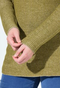 Olivgrüner, gestrickter Pullover mit vertikaler Rippstruktur und kontrastierenden Nähten an den Bündchen. Weiche Textur und lockere Passform, Hände, die die Ärmel anpassen.