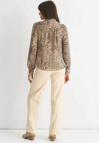 Leopard print blouse with a high collar, gathered detailing, and long puff sleeves, paired with beige wide-leg trousers and brown heeled boots.