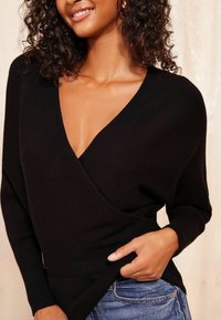 Zwart gebreid sweater met een diepe V-hals, geribbelde textuur en een losse pasvorm. Heeft lange mouwen en een licht gebogen zoom.