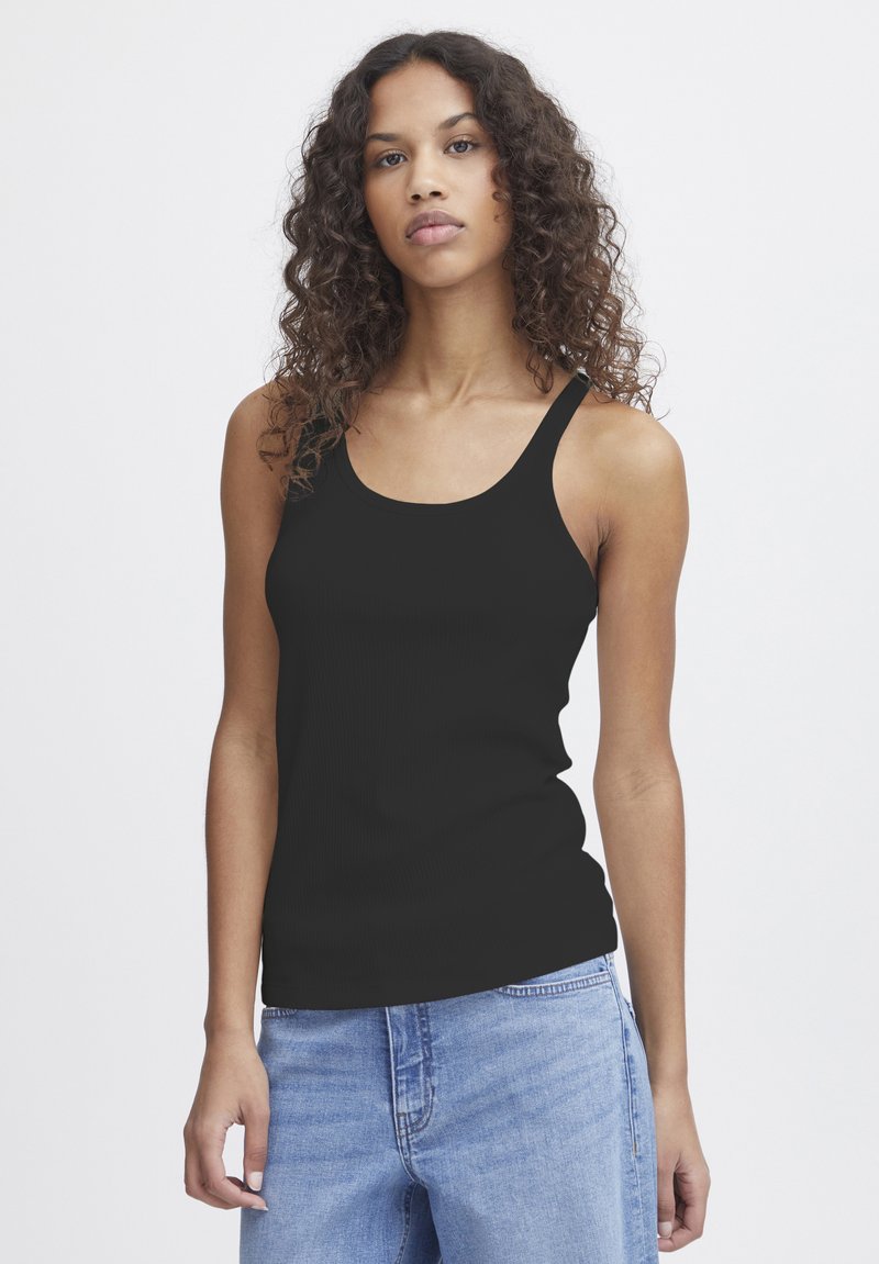 Zwarte geribbelde tanktop met dunne bandjes, een ronde halslijn en een aansluitende pasvorm; gecombineerd met lichtblauwe spijkerbroek.