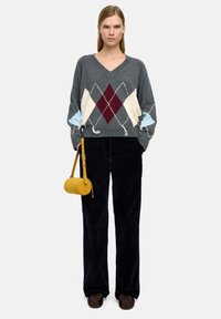 Szary sweter robiony na drutach z dekoltem w kształcie litery V, ozdobiony wzorem w romby w kolorach burgundowym, kości słoniowej i niebieskim. Połączony z ciemnymi spodniami z korduroju i żółtą torbą.