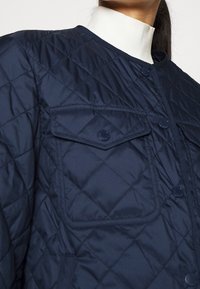 Giubbotto trapuntato navy con motivo a rombi, dotato di chiusura frontale con bottoni, due tasche sul petto e colletto alto. Materiale liscio e leggero.