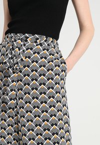 Pantalons larges à motifs présentant un design géométrique en noir, blanc et jaune, dotés d'une taille élastique et de poches latérales.