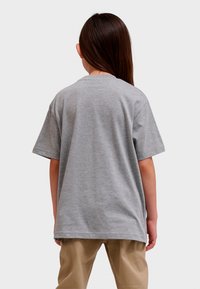 Grå bomulds t-shirt med korte ærmer; har en rund hals, en afslappet pasform og en glat overflade. Båret med beige bukser.