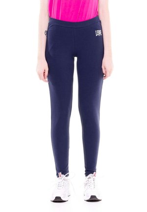 Mannequin portant un legging bleu marine taille haute orné d’un petit logo blanc, un haut rose vif et des baskets blanches sur un fond blanc uni.