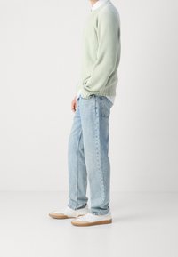 Maglione lavorato a maglia di un verde chiaro, jeans blu chiaro dal taglio morbido e sneakers bianche con dettagli marroni. Design semplice e casual per un outfit.