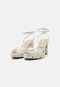 Sandalias blancas de tacón alto con estampado floral, tacones de bloque, plantillas acolchadas, puntera abierta y tiras en el tobillo con cierre de hebilla.