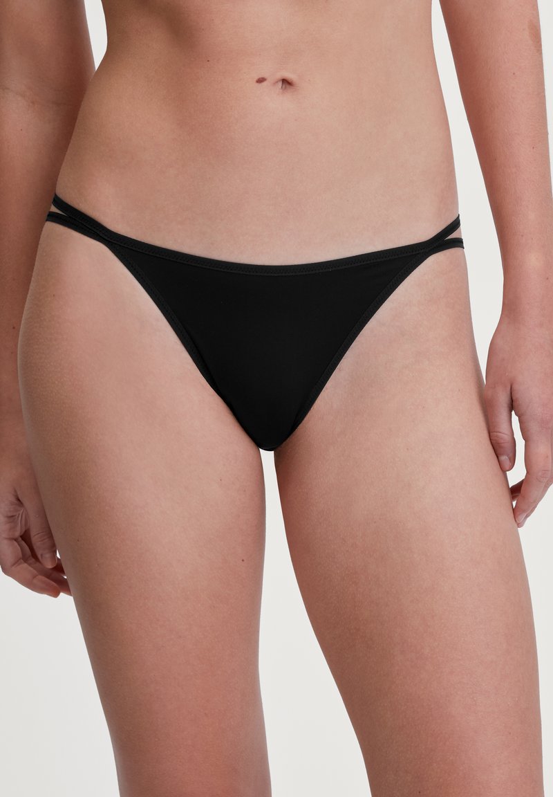 Zwarte bikini onderkant met een lage taille. Gemaakt van gladde stof, met dunne zijbandjes en minimale bedekking. Eenvoudige en naadloze afwerking.