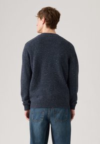 Mørkeblå strukturert genser med rund hals og ribbestrikkede ermer, kombinert med lyseblå denimjeans med baklommer.