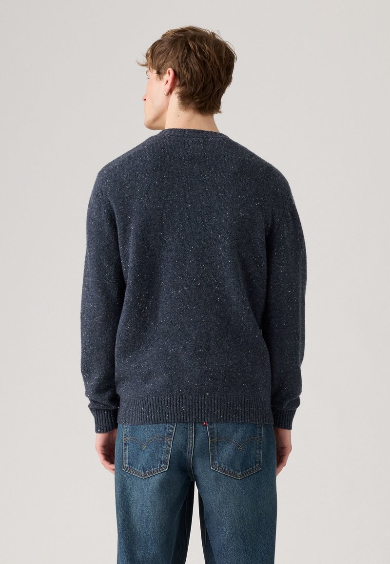 Marinblå strukturerad tröja med rund halsringning och ribbade ärmslut, parat med ljusblå denimjeans med bakfickor.