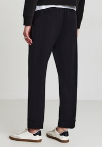 Schwarze Hosen aus glattem Material, mit lässigem Schnitt und Bündchen. Kombiniert mit weißen Sneakers mit schwarzen Akzenten.