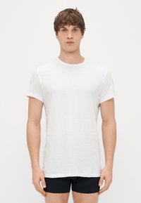 Balta medvilnės marškinėliai su apvaliu iškirpimu ir trumpomis rankovėmis, glotni tekstūra, prigludusi forma ir minimalistinis dizainas.