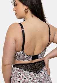 Soutien-gorge à motif floral en blanc, rose et noir, avec des bretelles ajustables noires et une finition en dentelle le long de la bande.