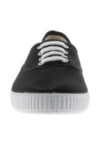 Baskets noires en toile avec semelle en caoutchouc blanche, dotées de lacets blancs, d'une pointe arrondie et d'une surface texturée. Design minimaliste.