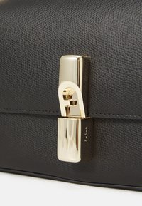Černá texturovaná kožená kabelka s lesklým zlatým zapínáním a elegantními liniemi, která zdůrazňuje moderní design a minimalistické akcenty.