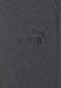 Mörkgrått tyg med svart Puma-logotyp som visar en hoppande puma och fet versaltext på ett klädesplagg.