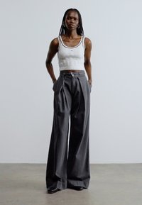 Šedé široké kalhoty s texturovaným povrchem, vybavené šňůrkou a bočními kapsami, spárované s přiléhavým bílým žebrovaným crop topem.