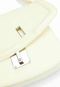 Borsa a tracolla in pelle crema con chiusura a patta, dotata di una fibbia rettangolare metallica e dettagli di cucitura. Texture liscia, design minimal.