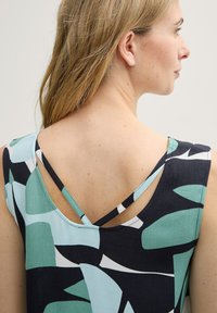 Multikleurige mouwloze top met een geometrisch patroon in teal, zwart en wit. De achterkant heeft een unieke dubbele bandontwerp.